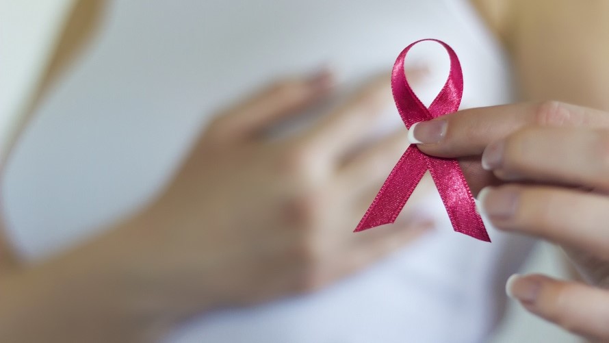 Weibliche Hand hält rosa Schleife gegen Brustkrebs Weibliche, linke Hand hält rosa Schleife gegen Brustkrebs, während recht Hand auf Brust liegt